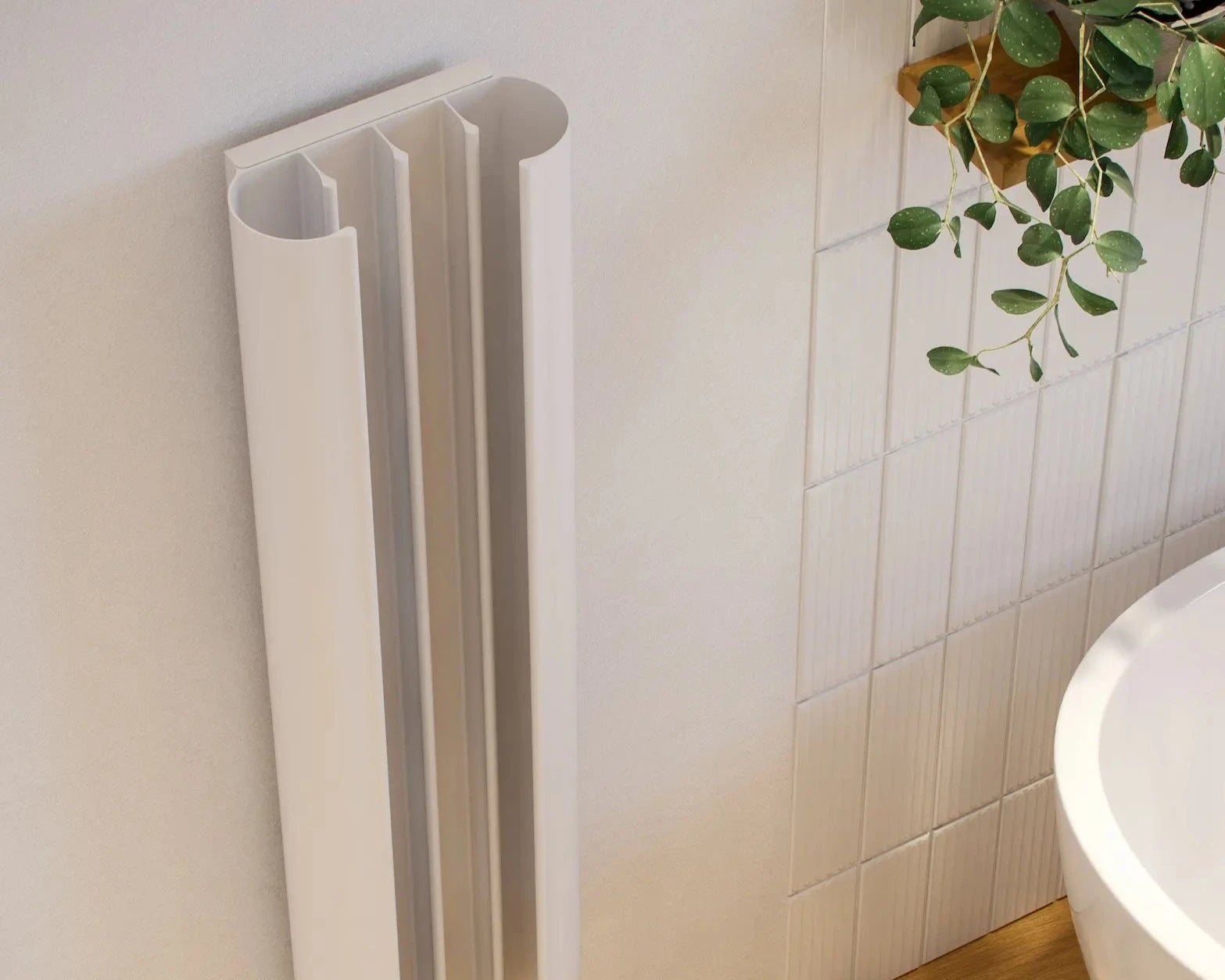 A white, loop-shaped heated towel rail mounted on a wall next to a bathtub with curved fins extending from its base.